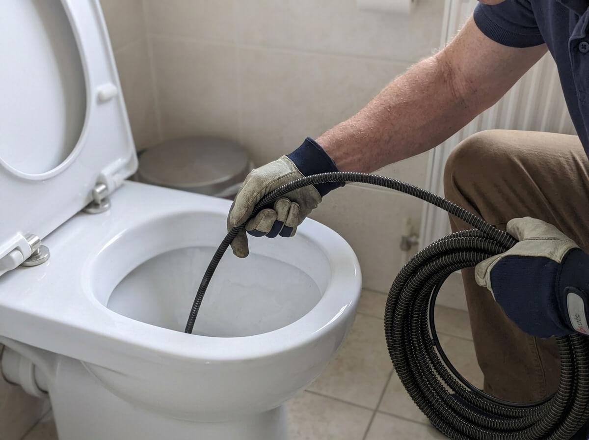 Philip clearing a blocked toilet with a drain auger